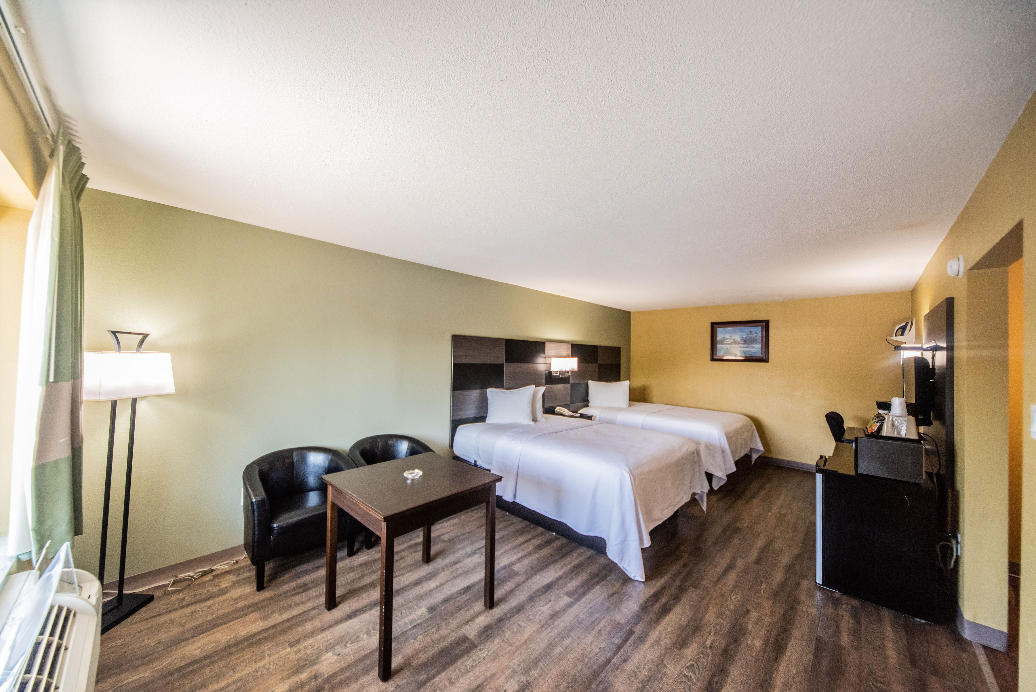 A hotel room with two beds, a desk, a chair, a desk lamp, a coffee machine, and a TV.