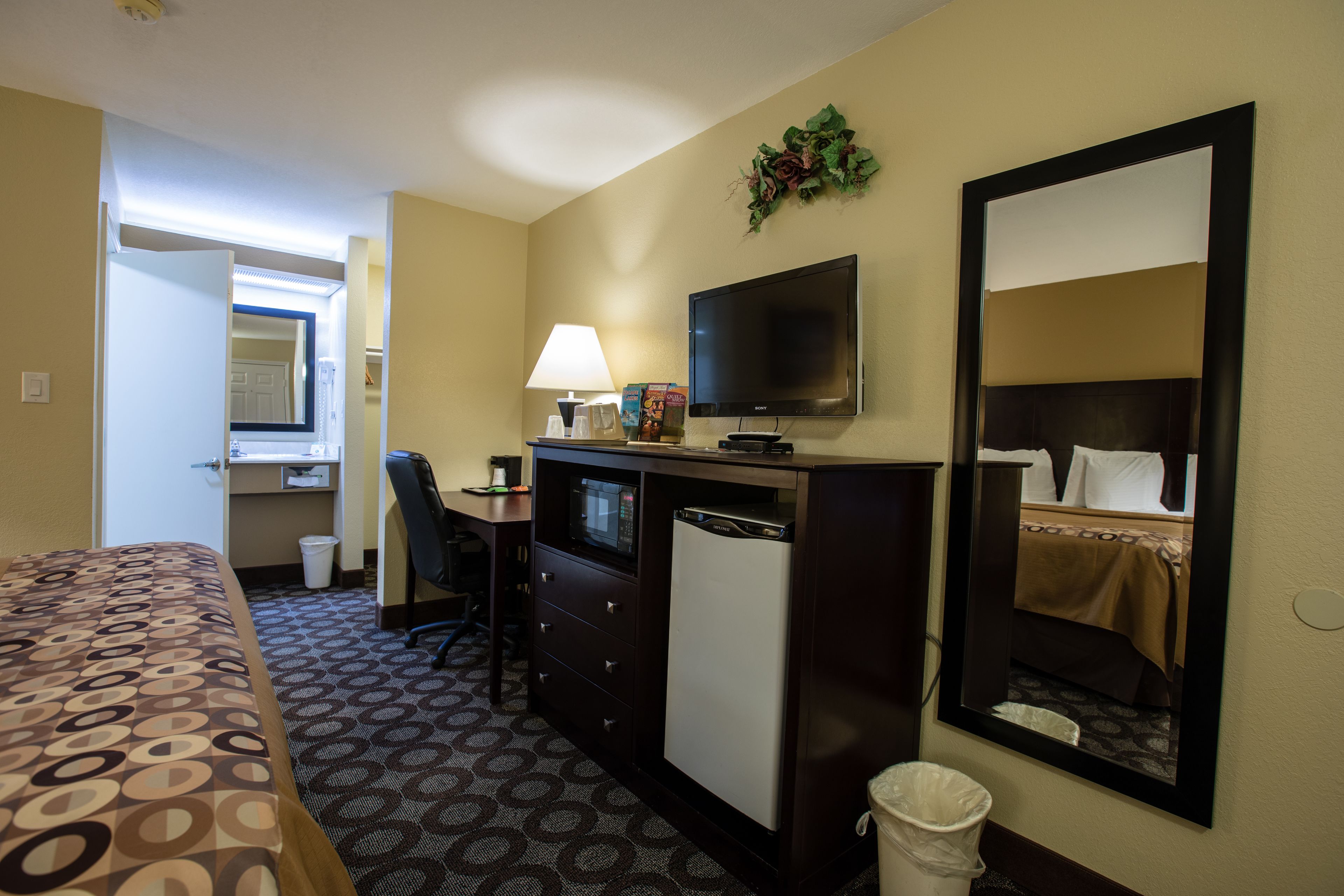 Una habitación de hotel con cama, escritorio, televisor y espejo.