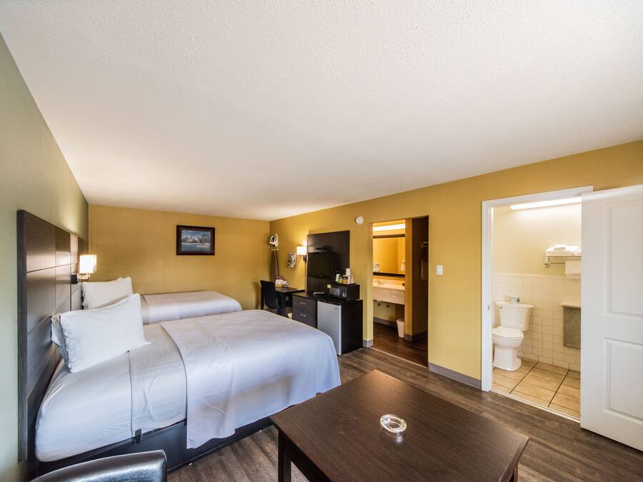 Ein Hotelzimmer mit zwei Betten, einem Schreibtisch, einem Stuhl, einem Fernseher und einem durch eine offene Tür einsehbaren Badezimmer.