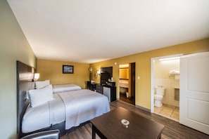 A hotel room with two beds, a desk, a chair, a TV, and a bathroom visible through an open door.