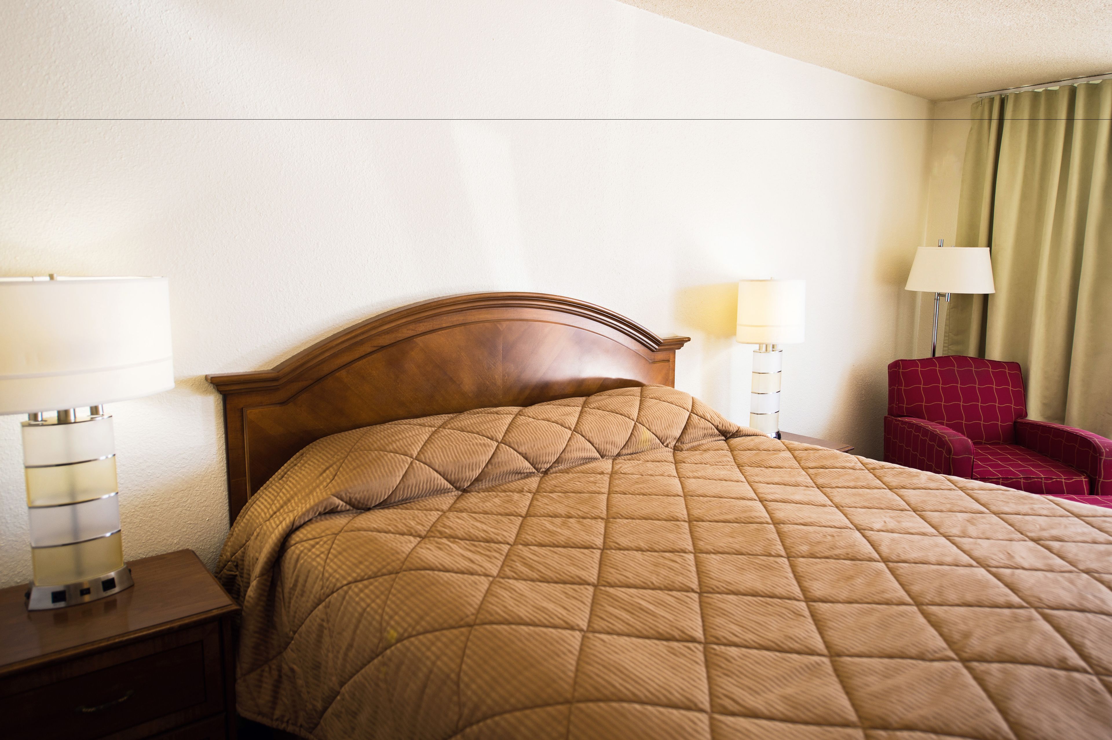 A hotel room with a bed, two bedside lamps, a red chair, and a nightstand.