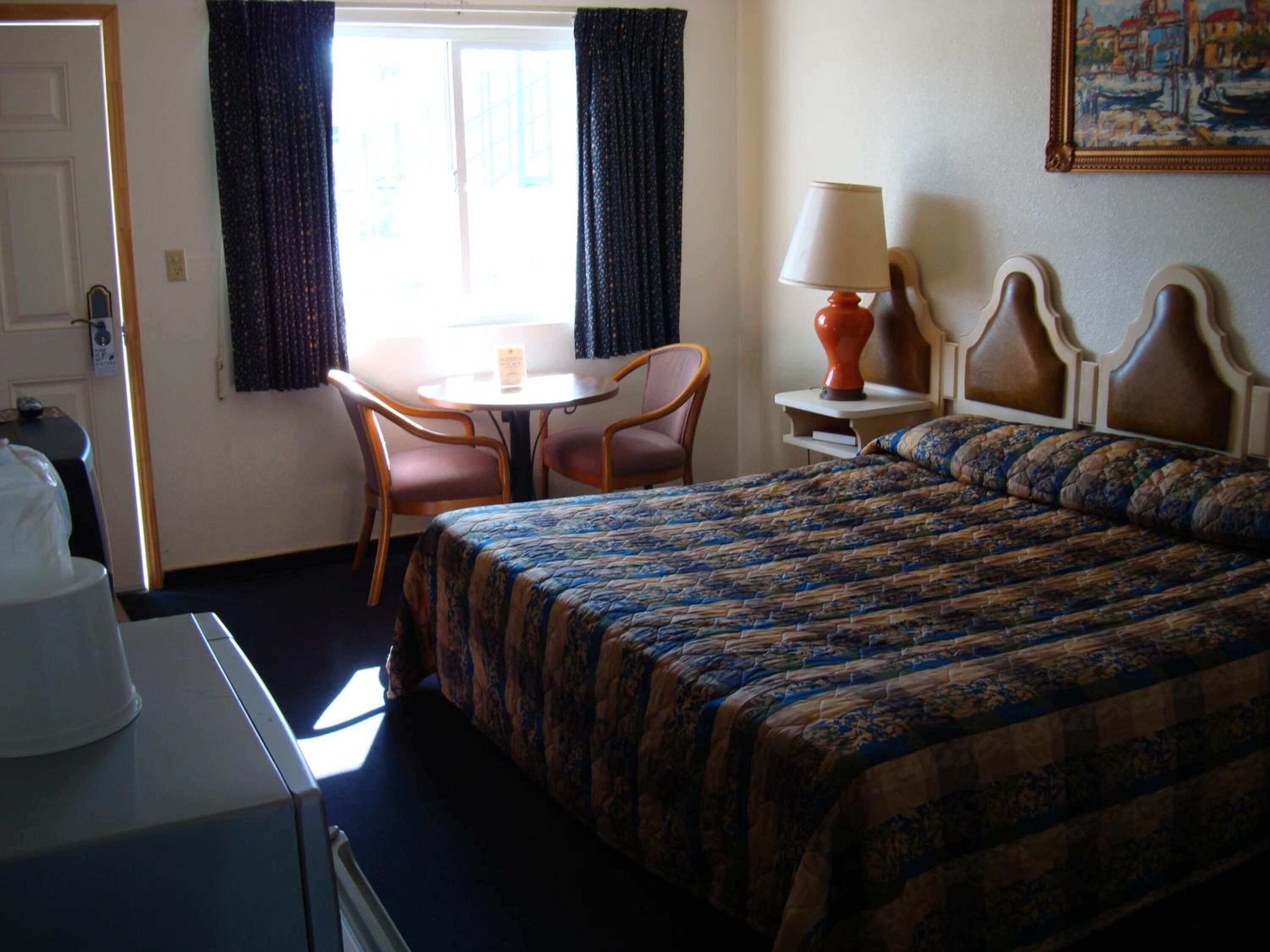 A hotel room with a bed, a desk, a chair, a table, and a lamp.