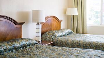 A hotel room with two beds, a nightstand, a lamp, and a window with curtains.