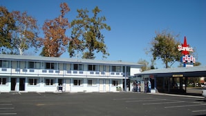 Un motel con un edificio de dos pisos, un área de estacionamiento techada y un letrero rojo llamativo.
