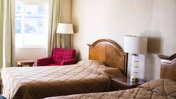 A hotel room with two beds, a red armchair, a lamp, and a view of the outside.