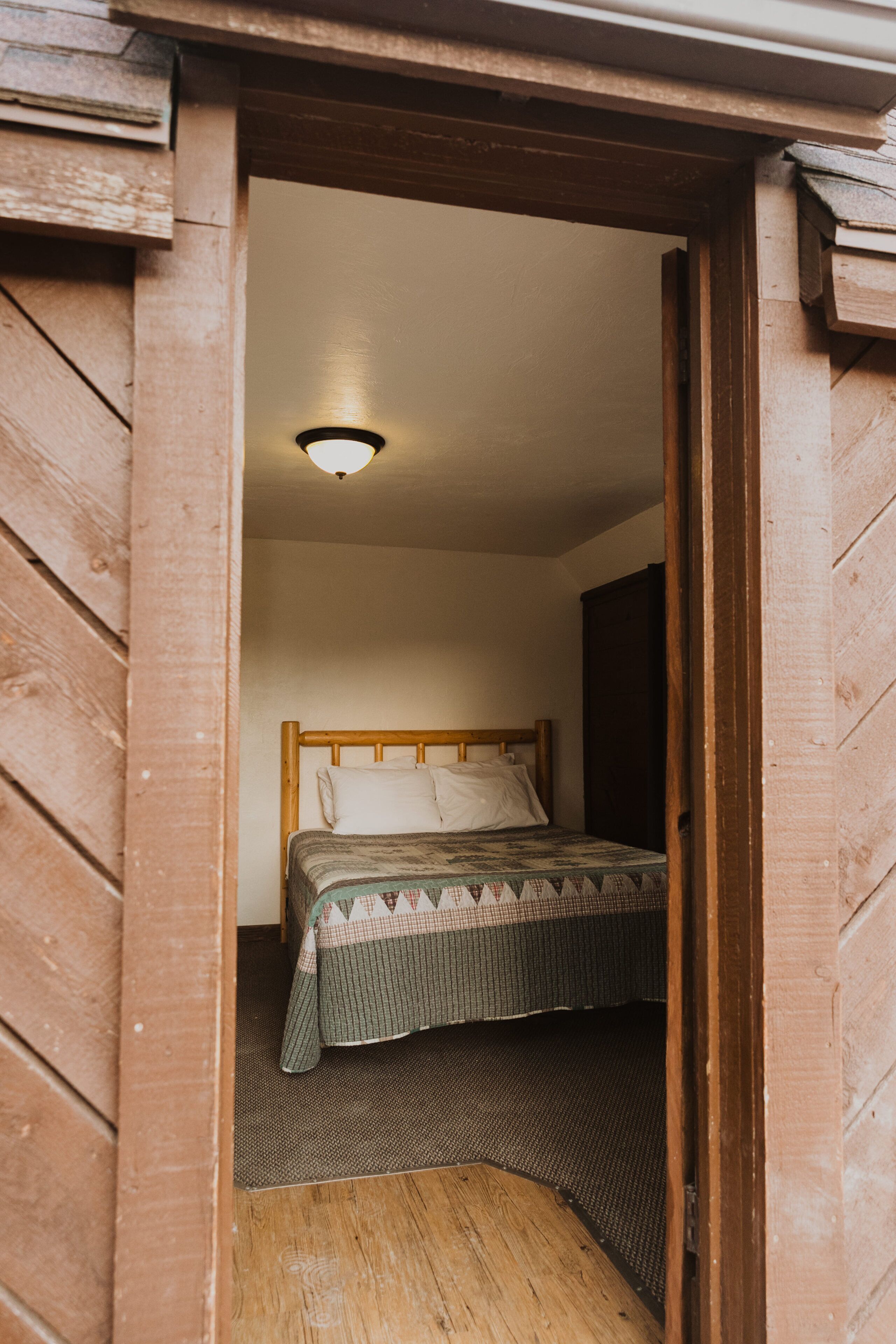 A small, cozy room with a wooden bed, a headboard, and a ceiling light.
