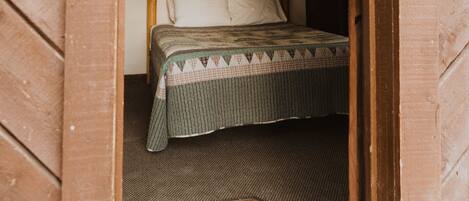 A small, cozy room with a wooden bed, a headboard, and a ceiling light.
