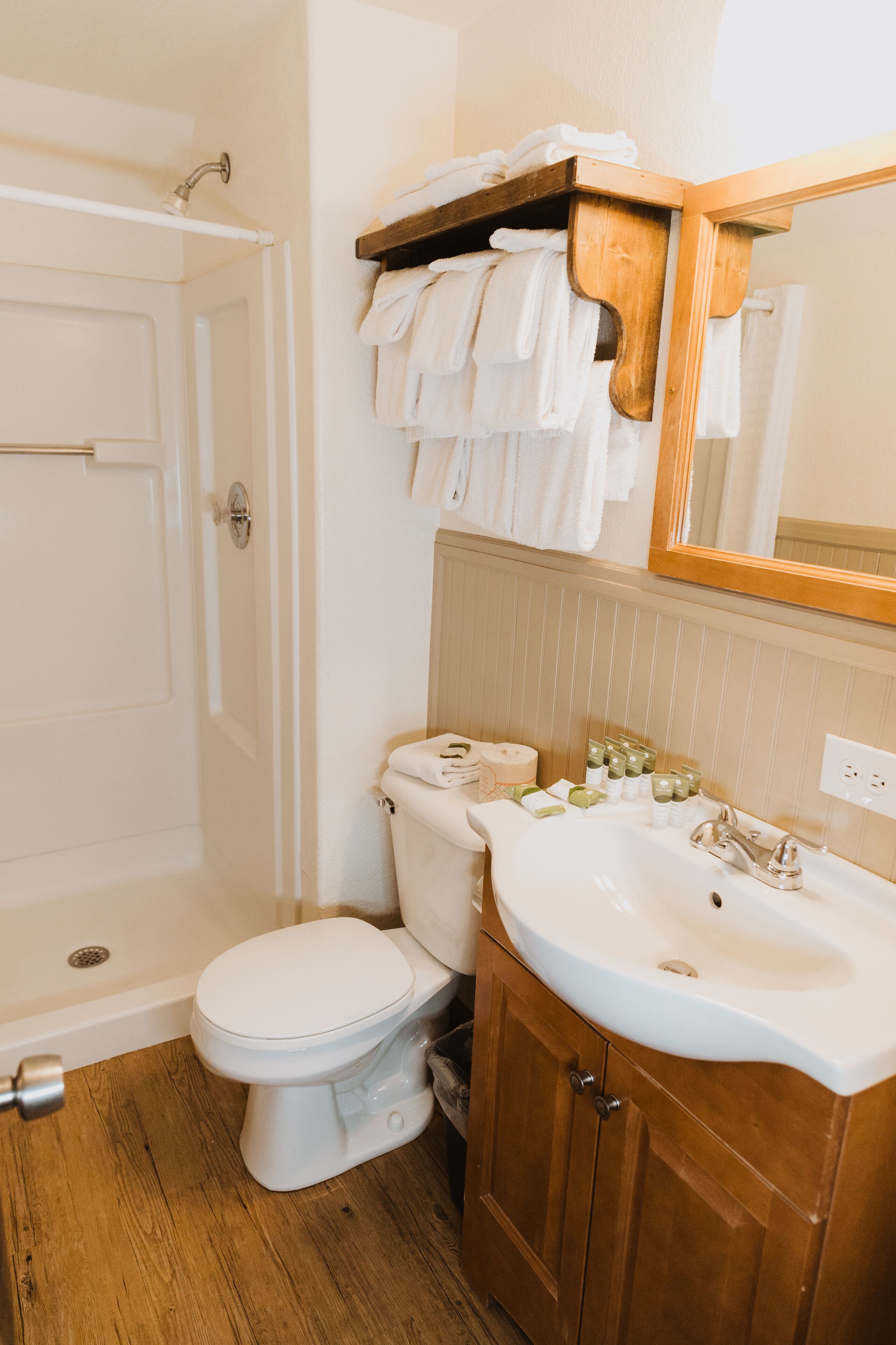 A bathroom with a toilet, sink, and shower. There is a towel rack above the toilet and a mirror above the sink.