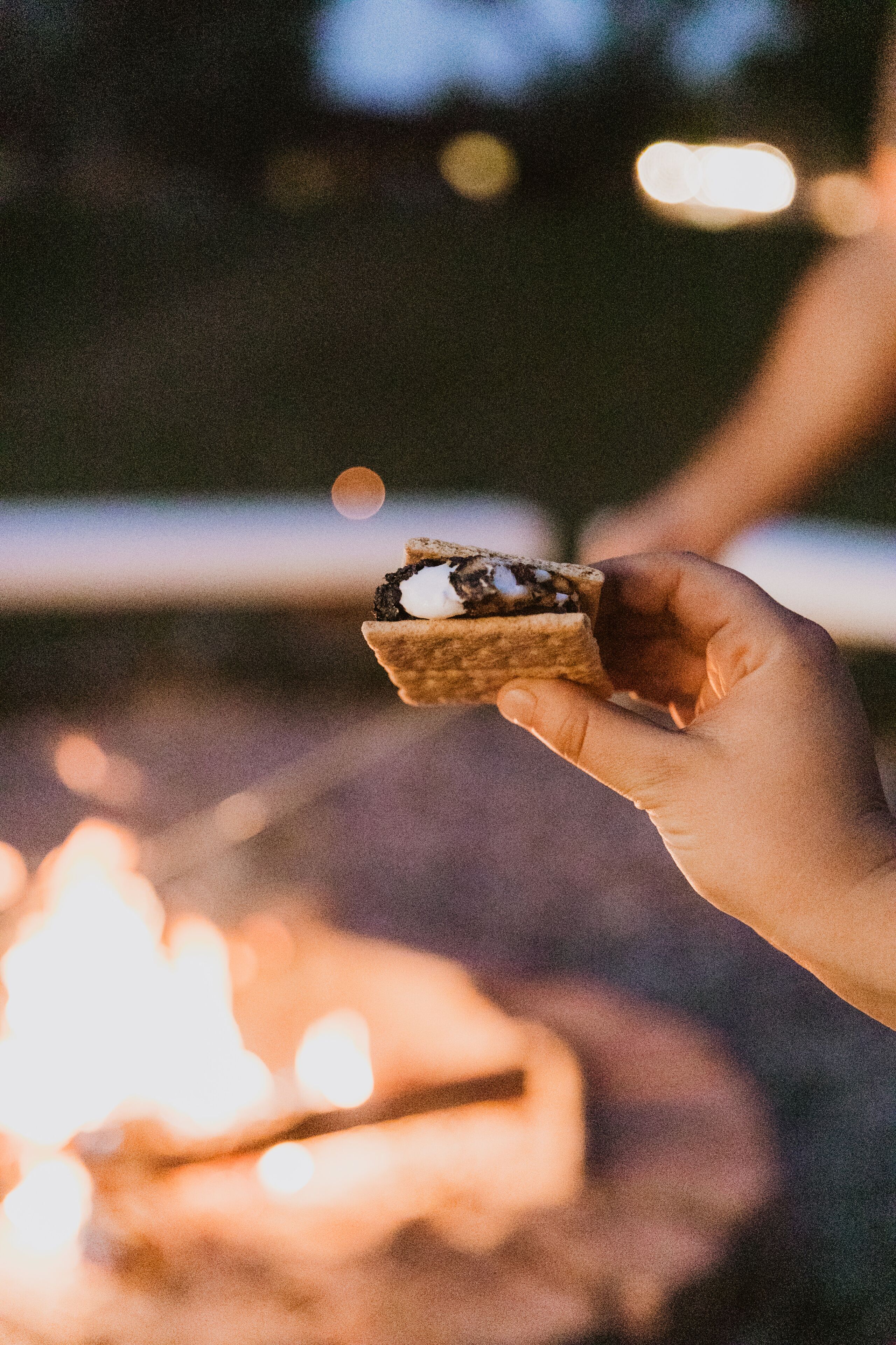 A hand holding a dessert near a campfire.