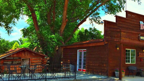 A rustic Pioneer Museum building with a wooden facade, a sign for the Bryce Pioneer Motel, and outdoor seating. - Bryce Pioneer Village (Tropic)