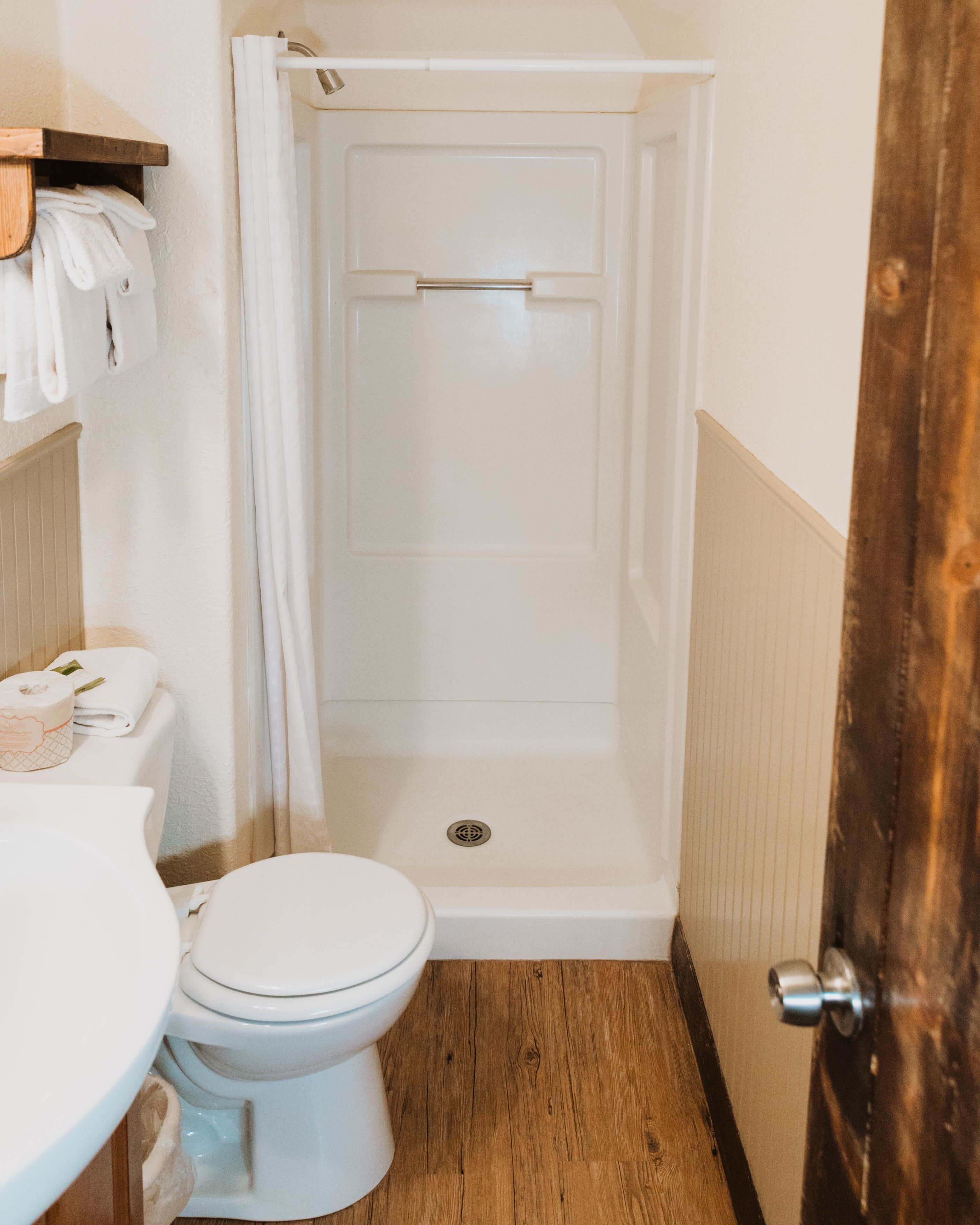 A bathroom with a white toilet, a shower stall, and a wooden floor.
