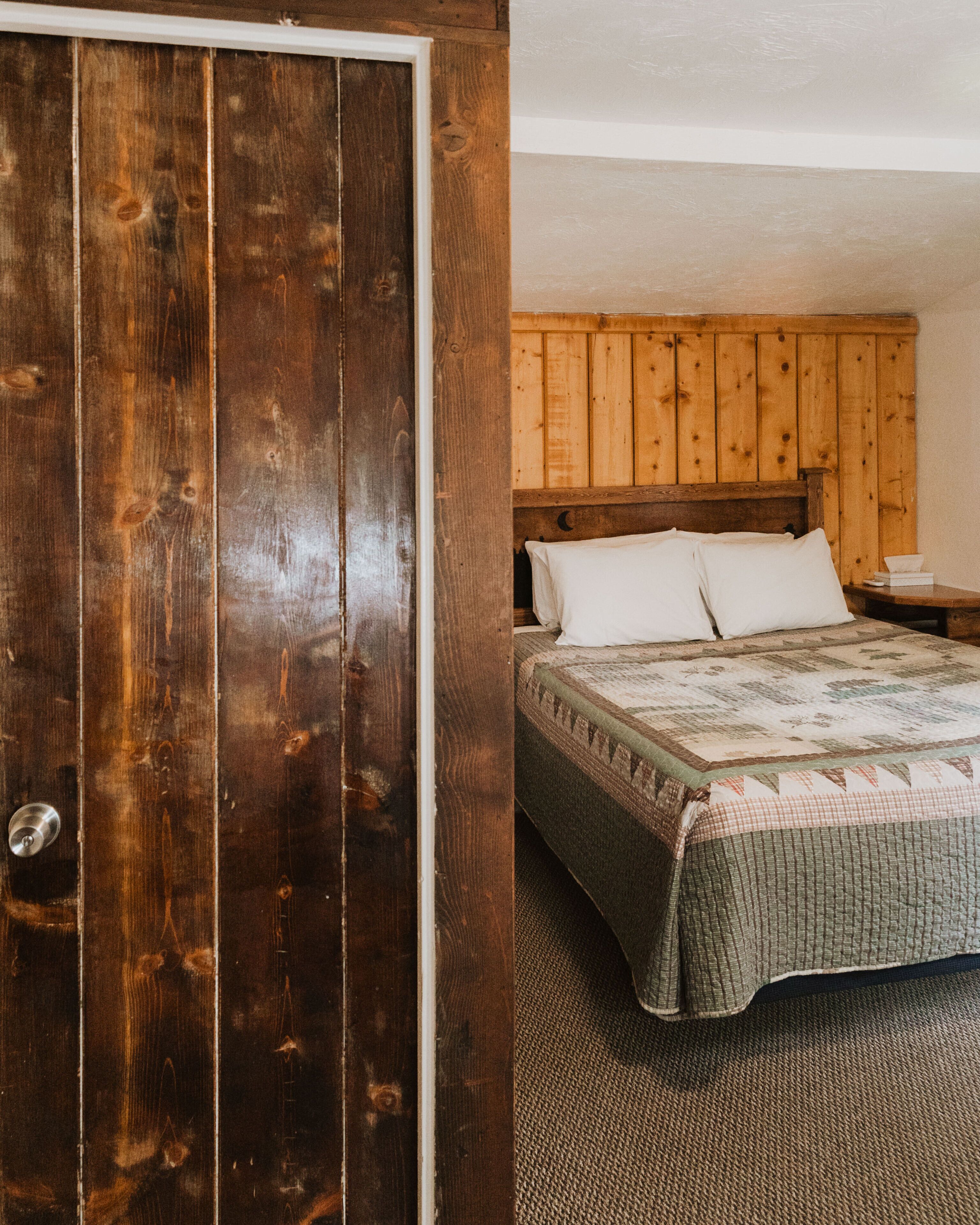 Un dormitorio con un armario de madera, una cama con colcha y una mesita de noche con un libro y una taza.