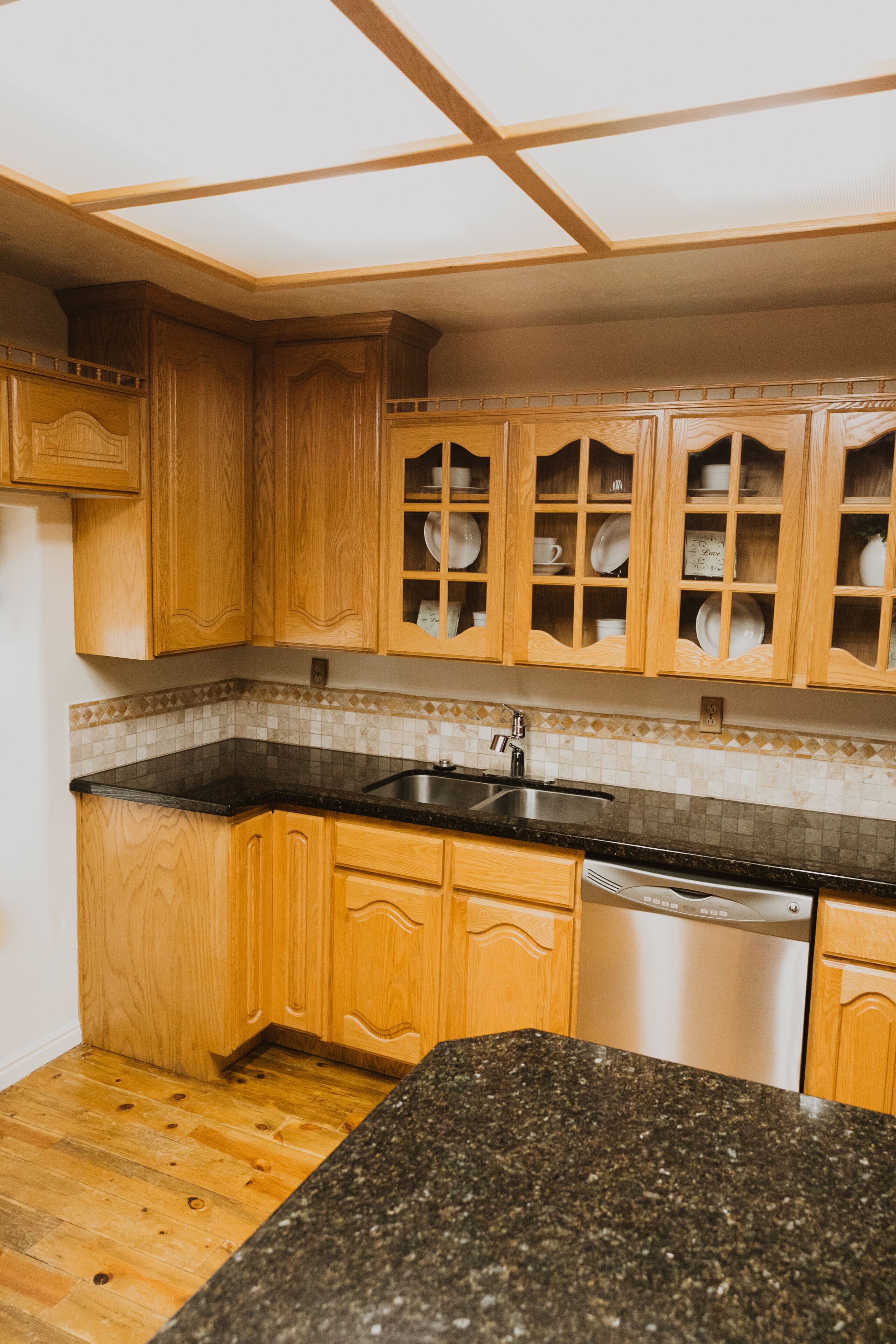 A kitchen with wooden cabinets, a granite countertop, and a stainless steel dishwasher.