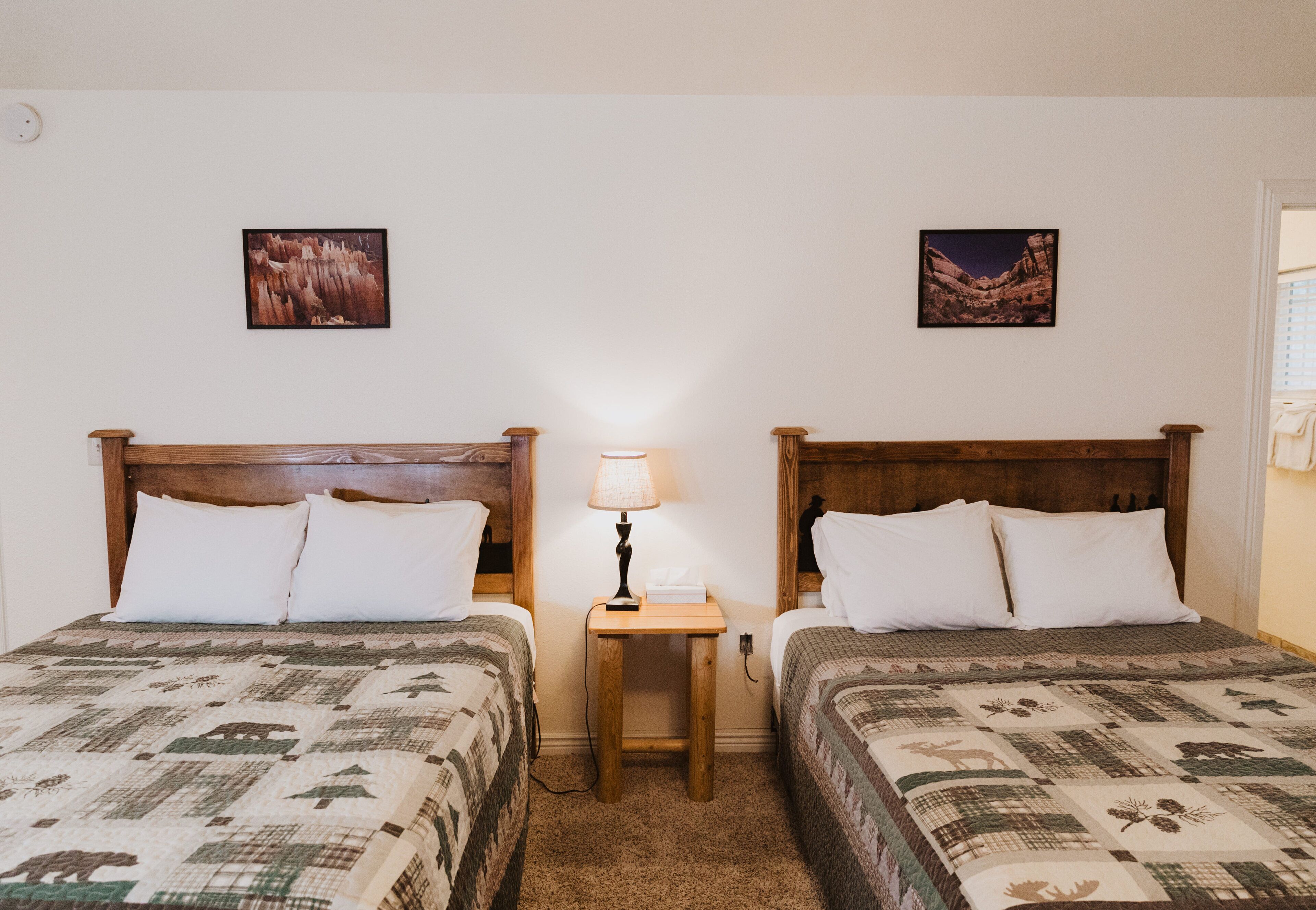 Habitación con dos camas, cada una con cabecero de madera, una mesita de noche con lámpara y un cuadro en la pared.