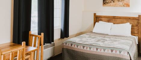 A bedroom with a wooden bed, a desk with a chair, black curtains, a window, and a painting on the wall.