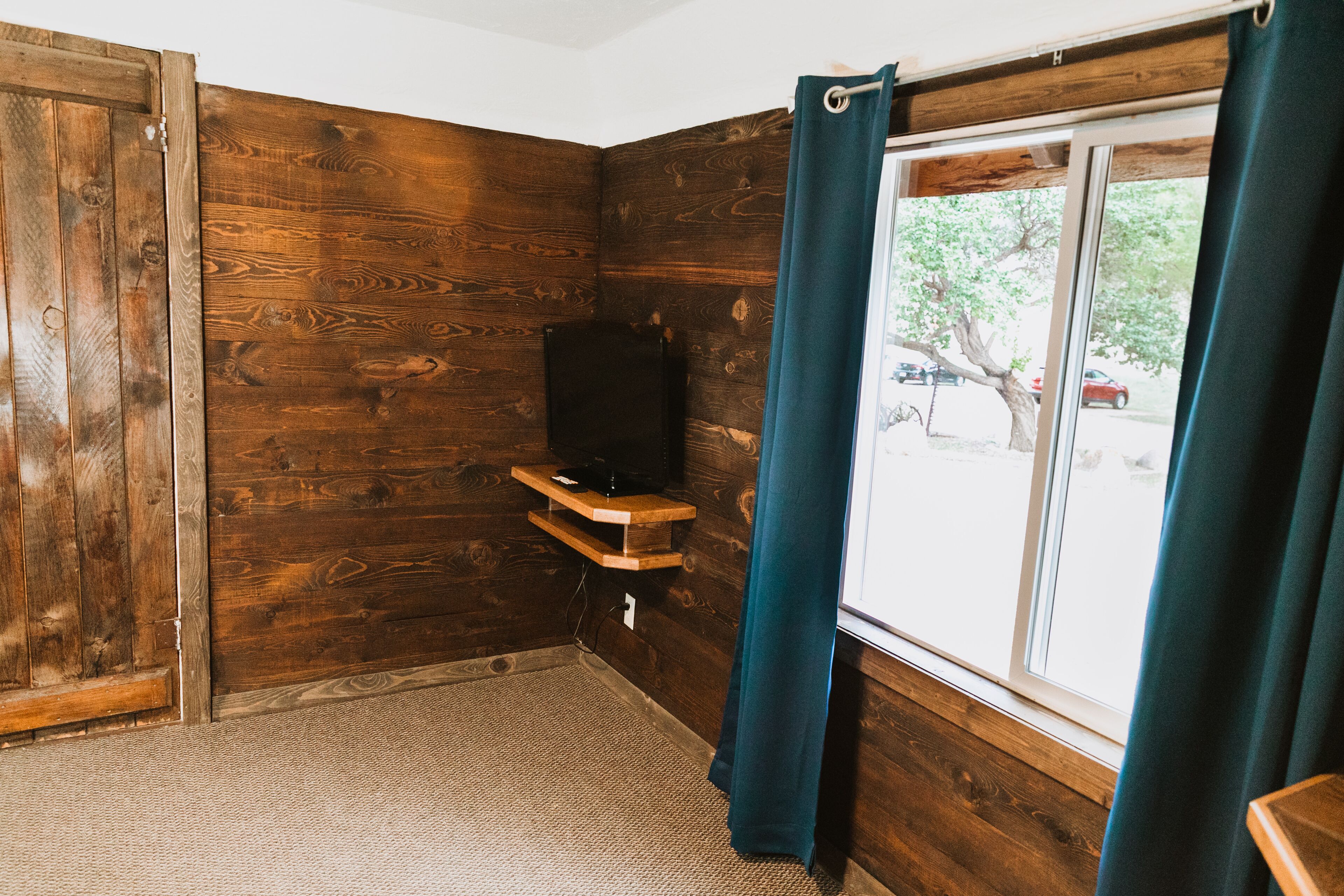 Una habitación con paredes de madera, una ventana con cortinas y un estante con televisor.