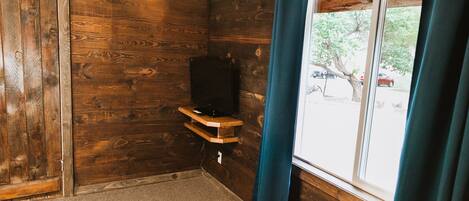 Una habitación con paredes de madera, una ventana con cortinas y un estante con televisor.
