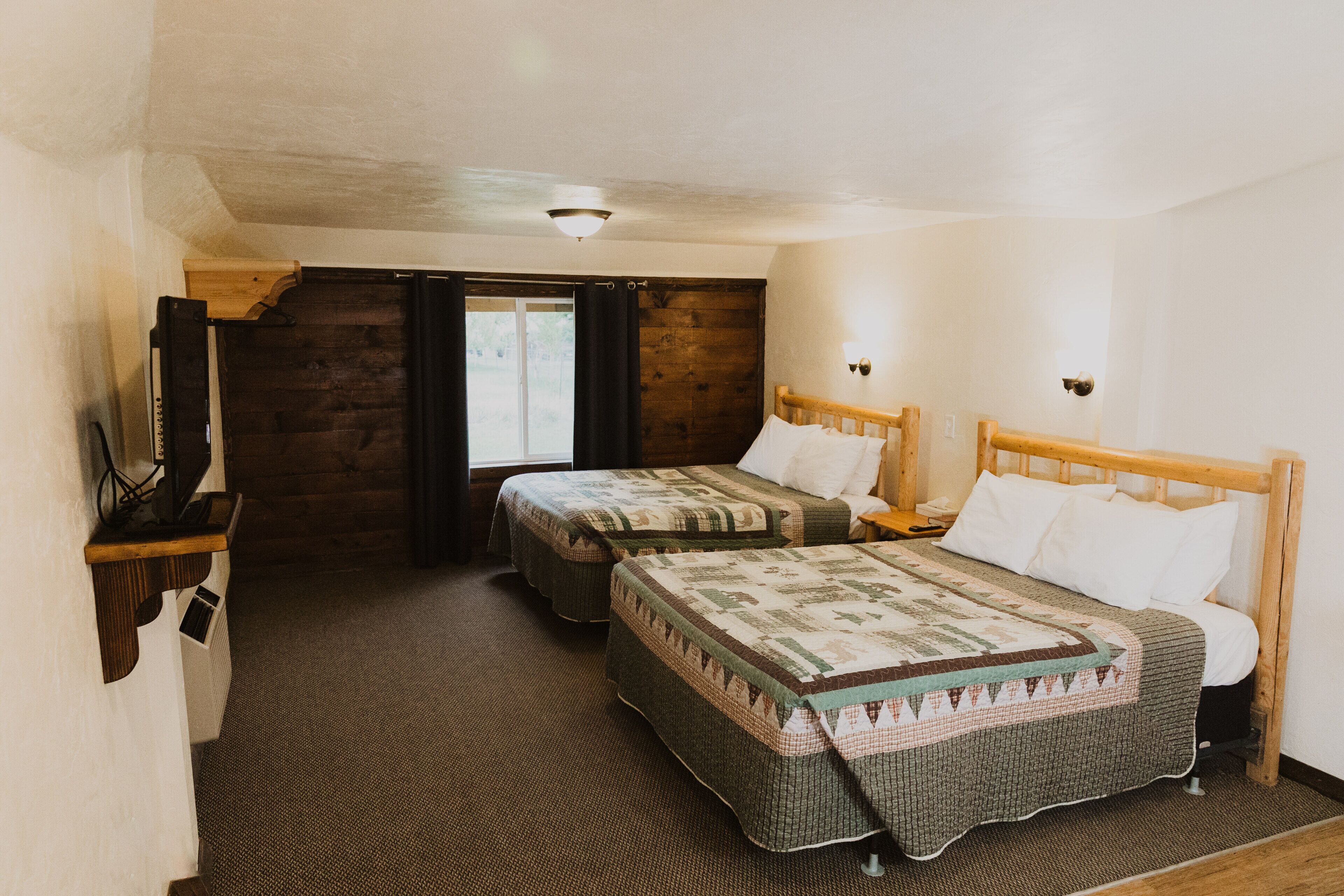 A room with two beds, a wooden headboard, a desk with a chair, and a television.