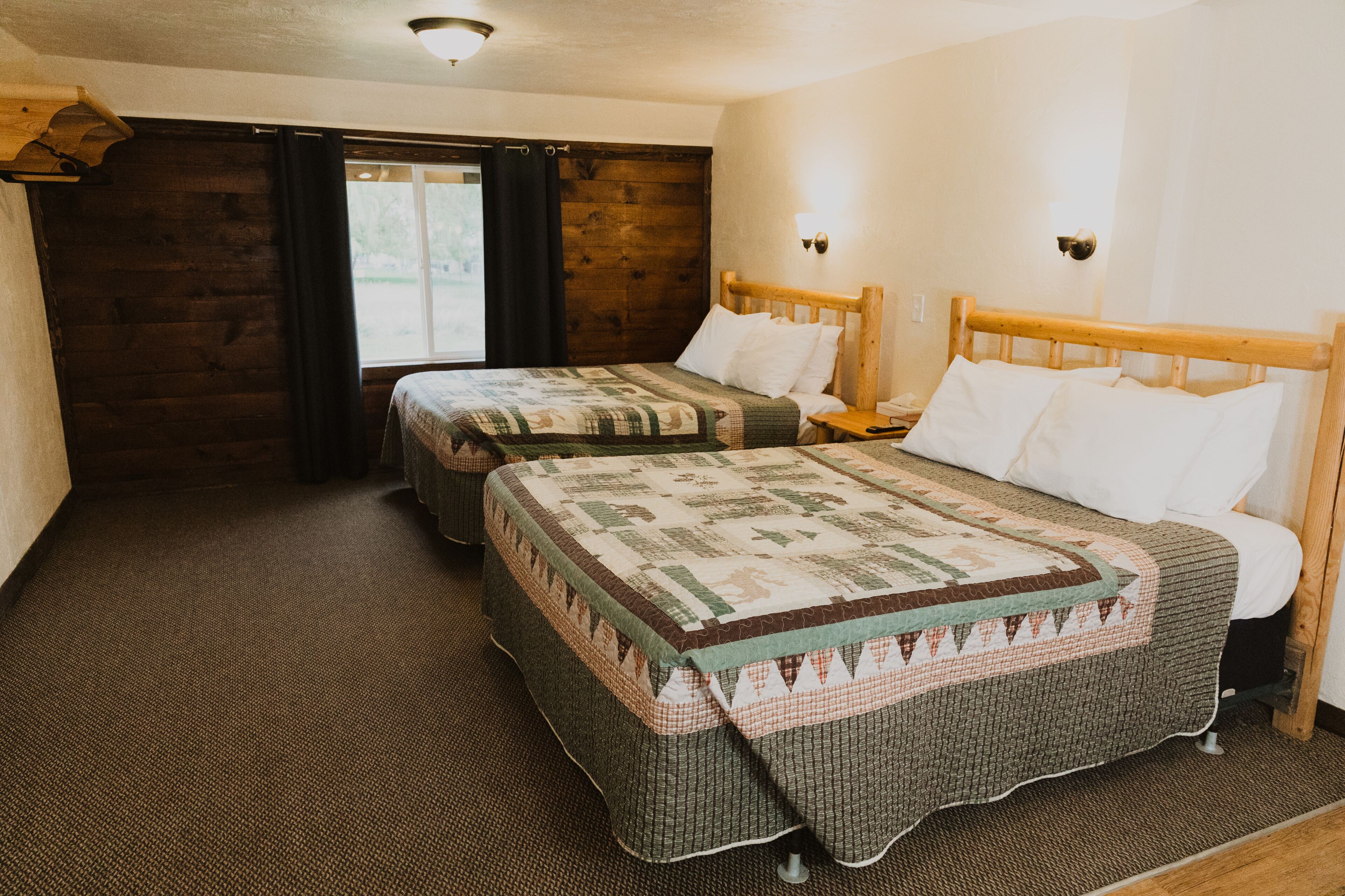 A room with two beds, wooden headboards, and a large window with curtains.