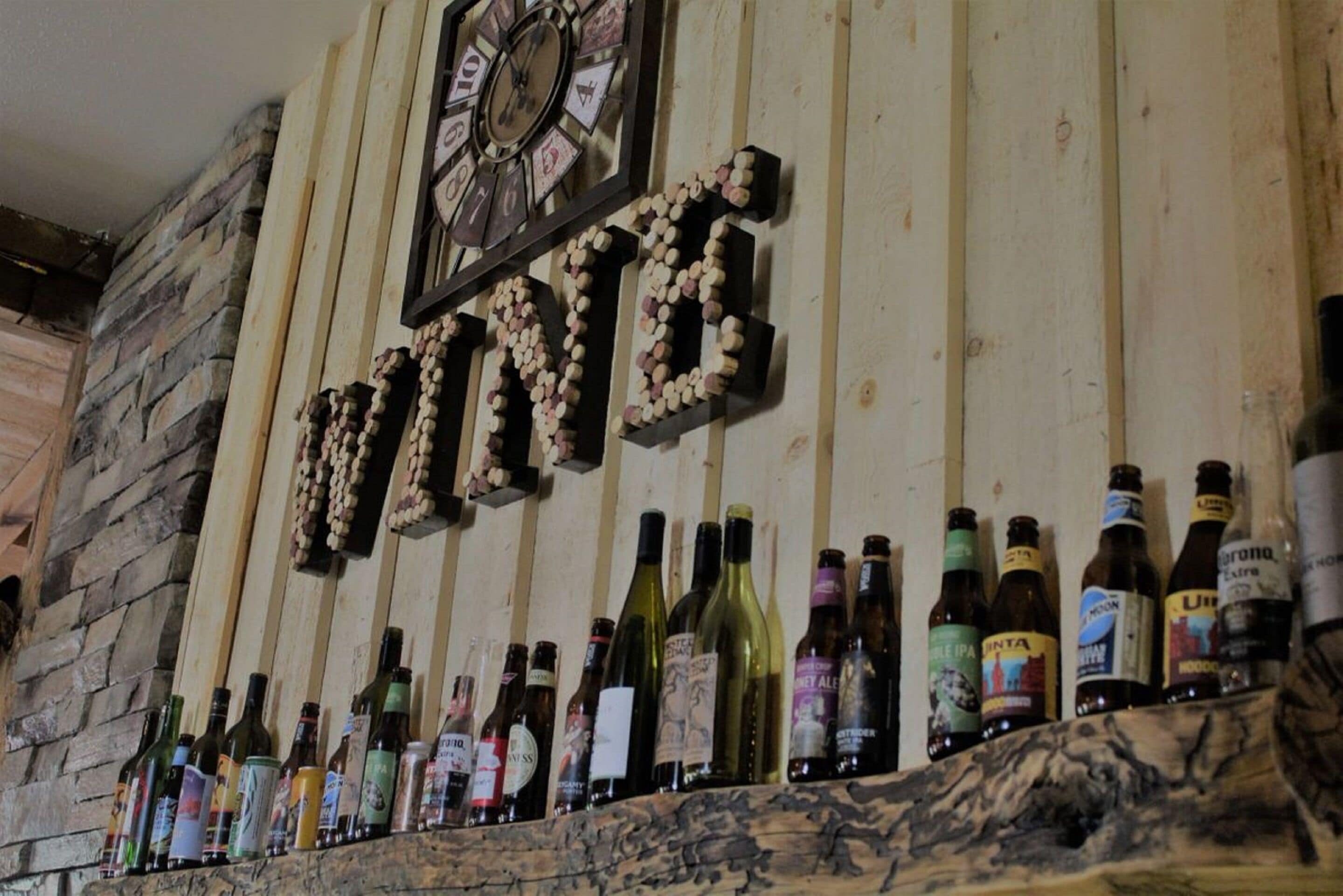 A wall with a clock and bottles of wine.