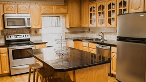 A kitchen with wooden cabinets, a central island with stools, a stainless steel refrigerator, and a microwave. - Bryce Pioneer Village (Tropic)