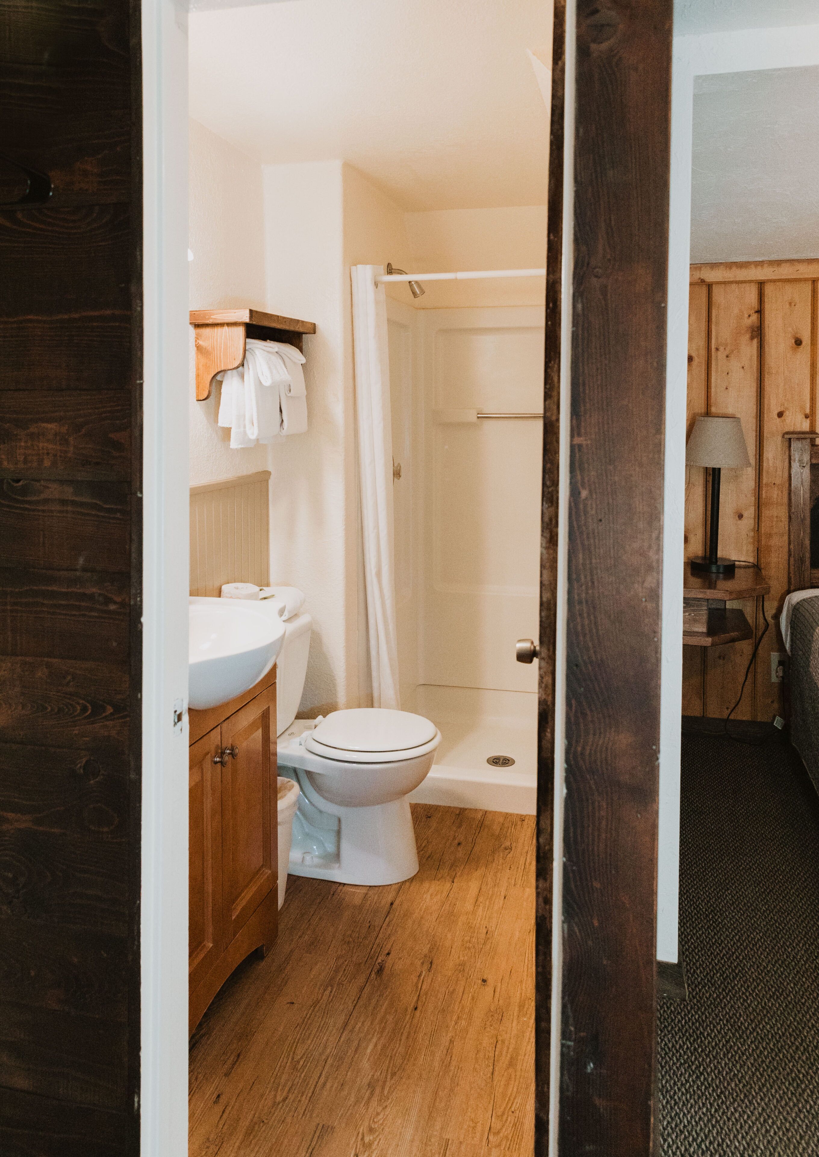 Une salle de bain avec un plancher en bois, des toilettes blanches, un meuble-lavabo en bois et un espace douche.