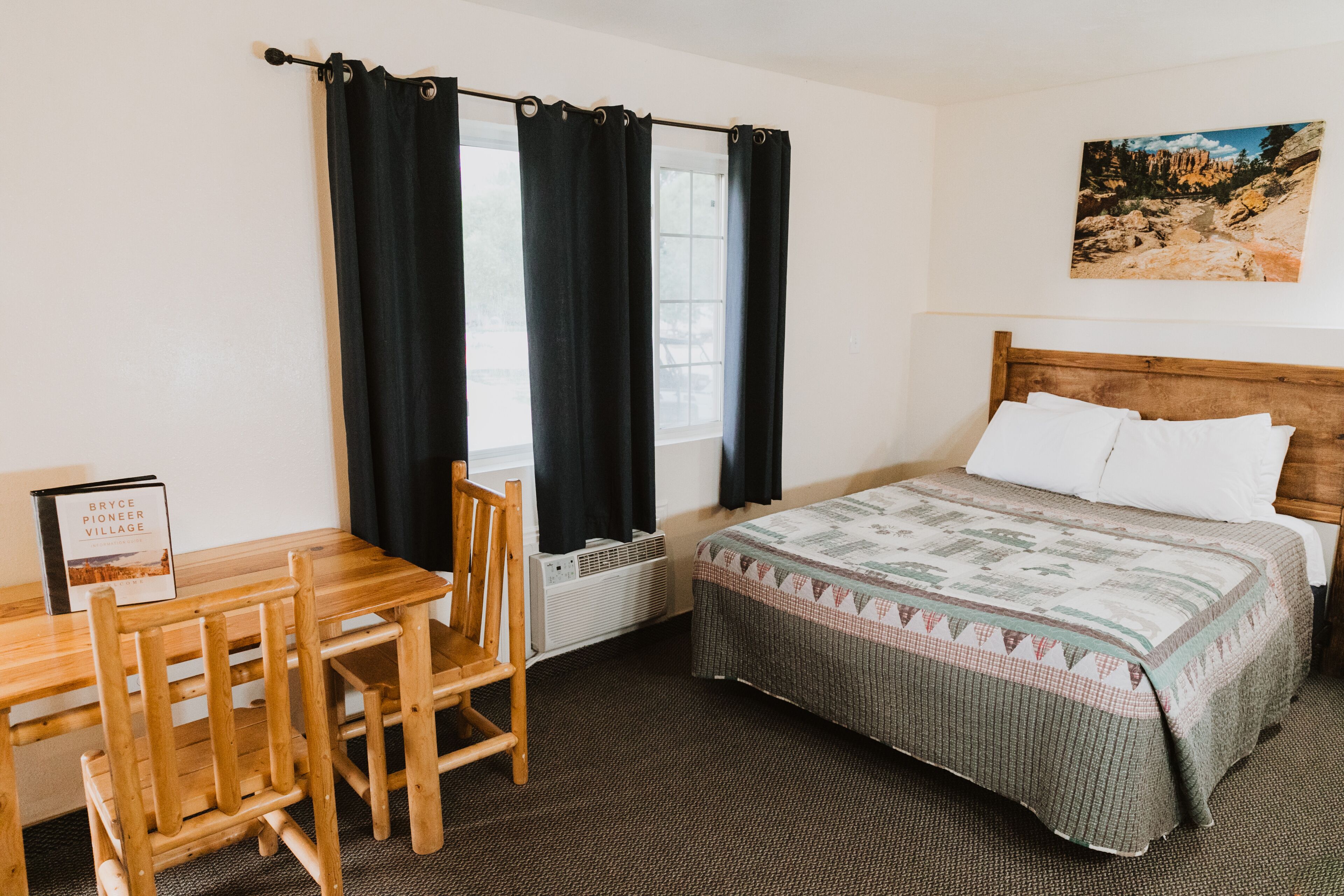Un dormitorio con una cama de madera, un escritorio con silla, una ventana con cortinas y un cuadro en la pared.