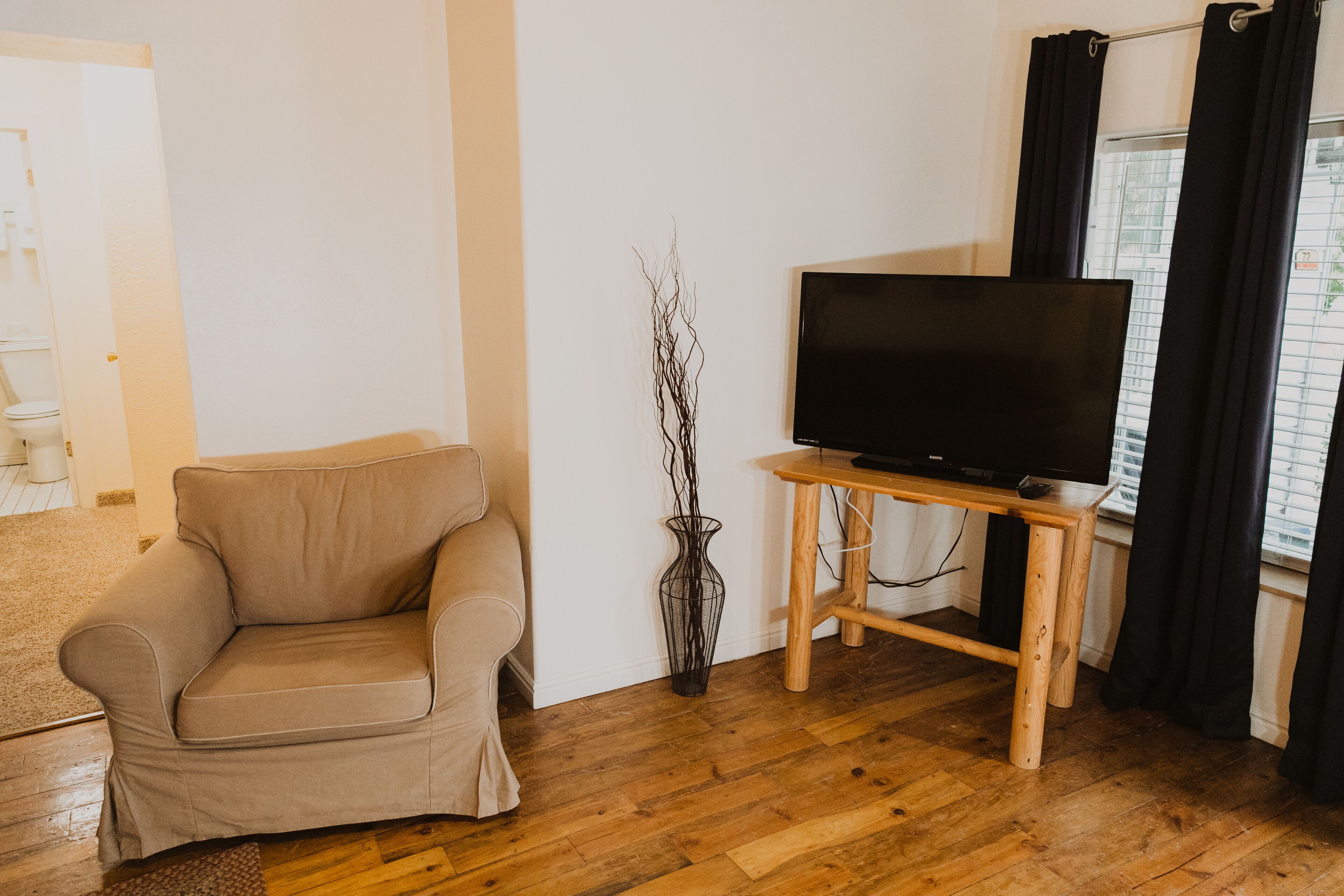 Ein Wohnzimmer mit einem beigen Sofa, einem Holzboden und einer schwarzen Vase.