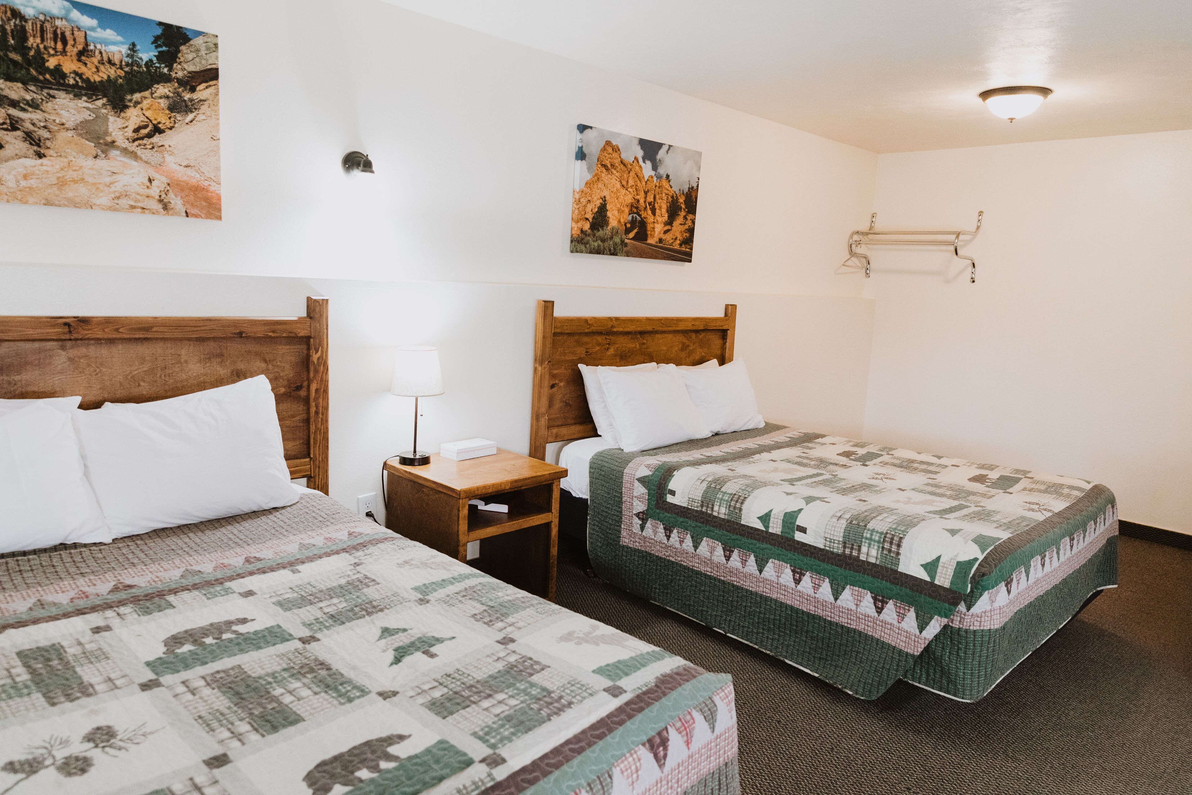 Une chambre d’hôtel avec deux lits en bois, une table de chevet, une lampe et deux porte-serviettes fixés au mur.