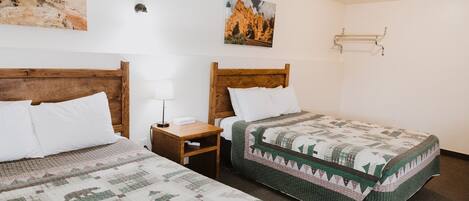 A hotel room with two wooden beds, a nightstand, a lamp, and two wall-mounted towel racks.