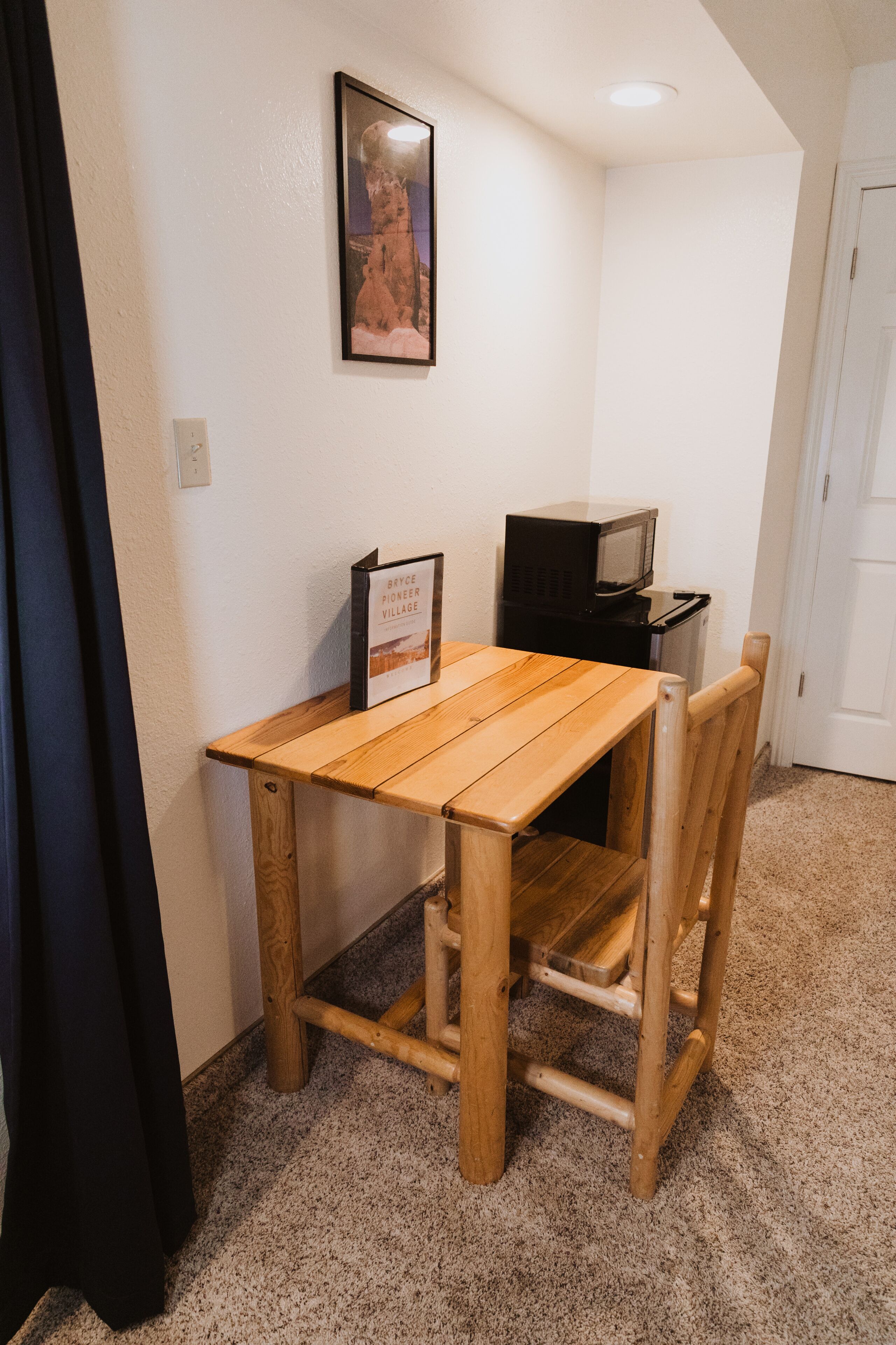 A small room with a wooden table, two chairs, a framed picture on the wall, and a microwave on a small table.
