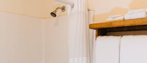 A bathroom with a bathtub, toilet, and a shelf with towels.