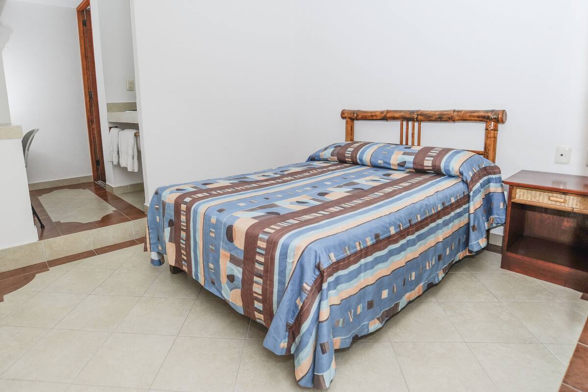 A bedroom with a bed, a wooden headboard, a bedside table, and a bathroom visible through an open door.