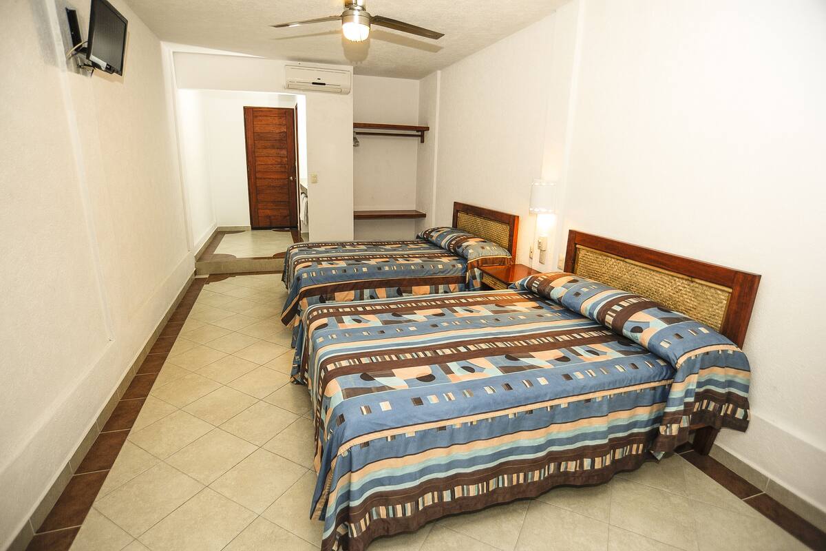 A hotel room with three beds, a ceiling fan, a TV, and a door leading to a hallway.