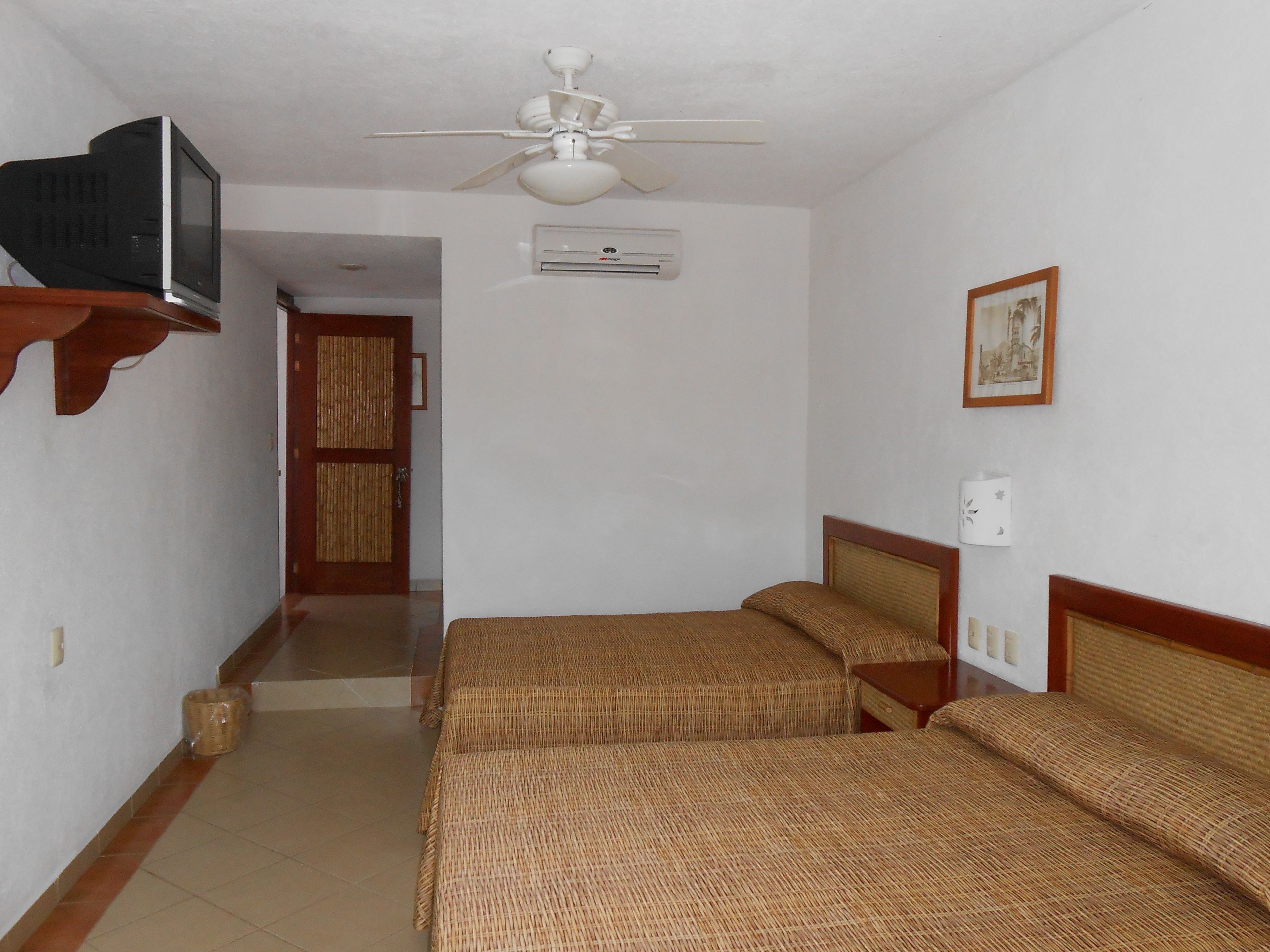 A room with two beds, a ceiling fan, an air conditioning unit, a television on a shelf, and a framed picture on the wall.