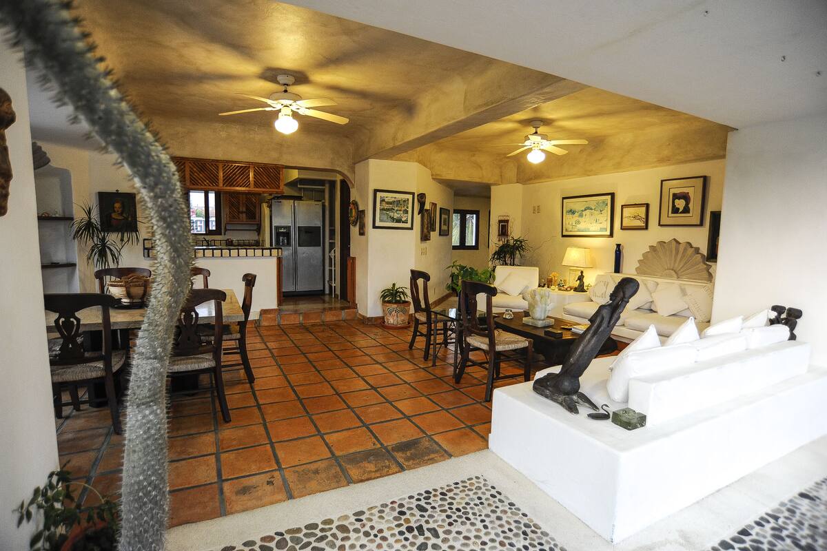 A spacious living area with a tiled floor, a dining table with chairs, a sofa, and ceiling fans.
