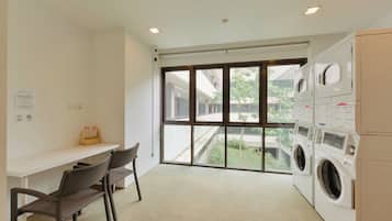 A laundry room with a large window, a white bench, and two washing machines.