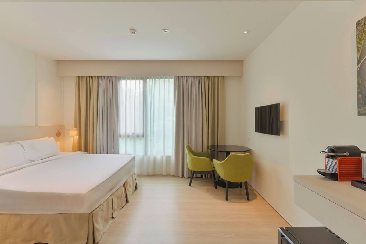 Une chambre d’hôtel avec un lit, un bureau avec des chaises, une télévision et un gril fixé au mur.