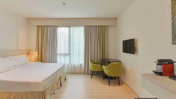 A hotel room with a bed, a desk with chairs, a television, and a grill on the wall.
