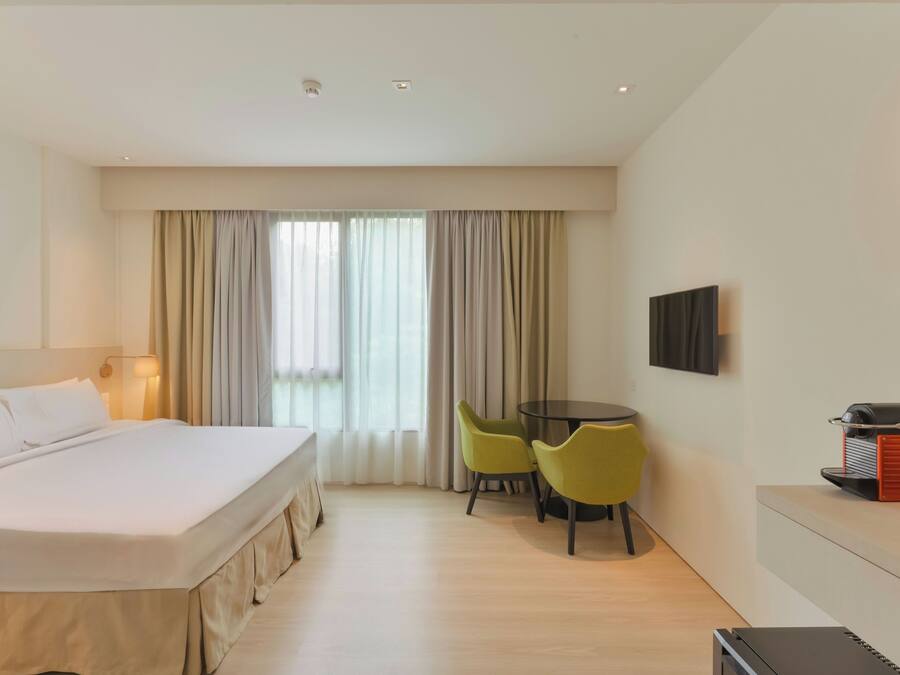 A hotel room with a bed, a desk with chairs, a television, and a grill on the wall.
