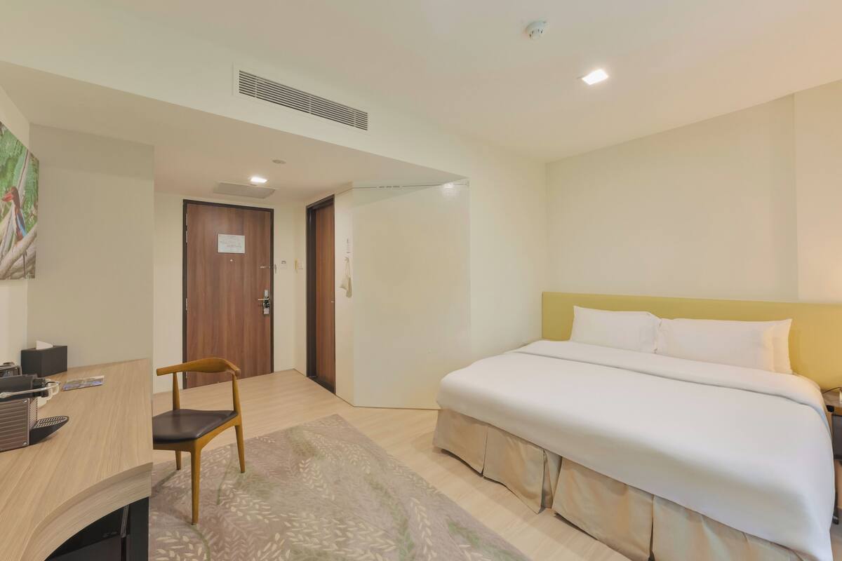 Une chambre d’hôtel avec un lit, un bureau, une chaise et une porte.