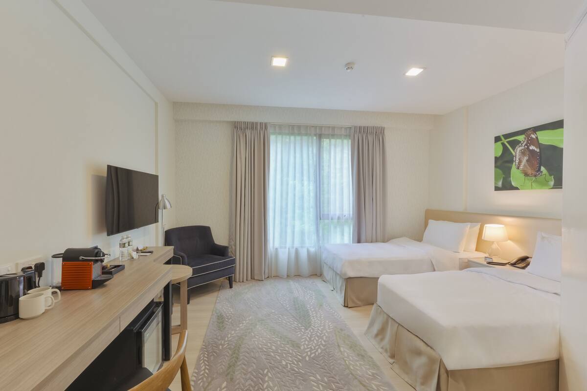 Une chambre d’hôtel avec un lit, un bureau équipé d’une machine à café, une télévision et une fenêtre avec des rideaux.