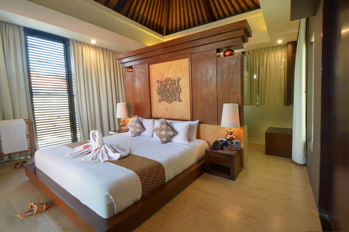 A large bed with a wooden headboard, two bedside tables with lamps, a large mirror, and a towel on the bed.