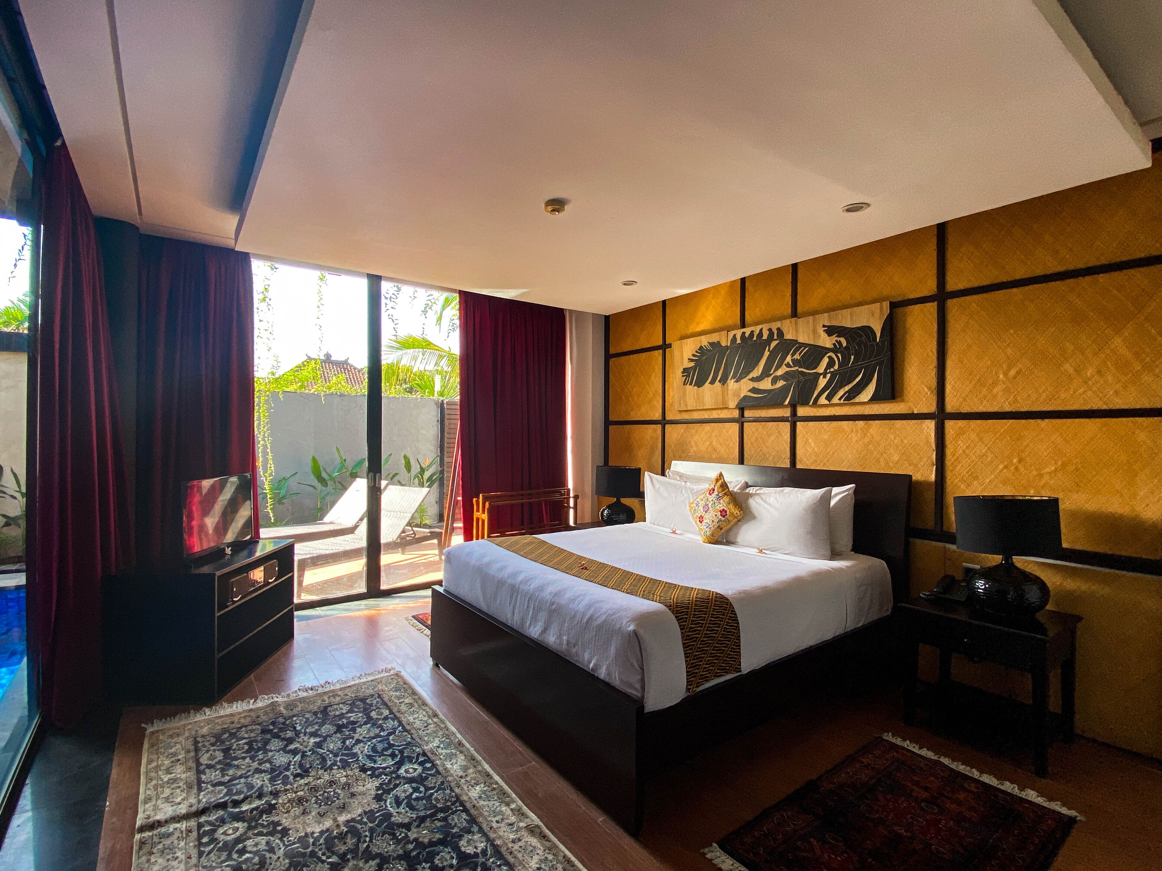 A modern hotel room with a large bed, a nightstand, a TV, and a view of the outdoors.