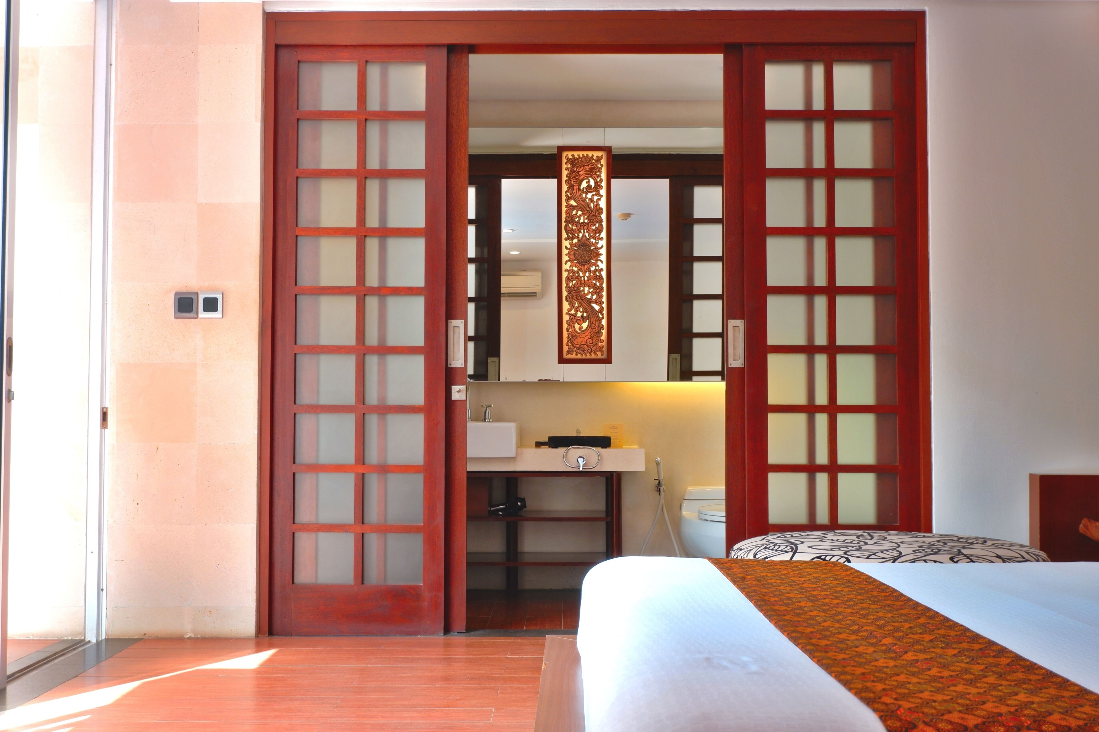 A hotel room with a bed, a desk with a sink, and a sliding door with frosted glass panels.