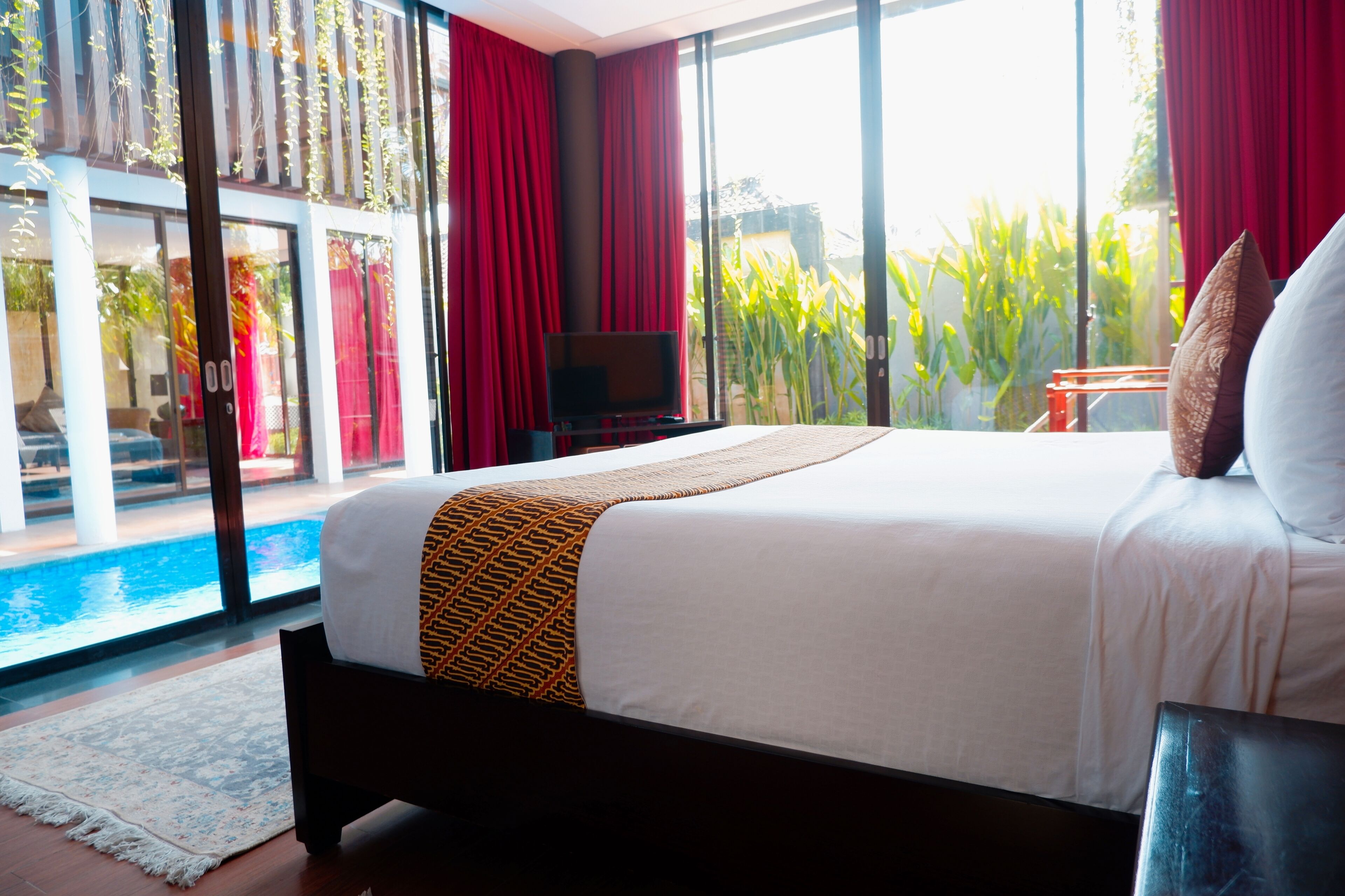 A hotel room with a large bed, a TV, and a view of a swimming pool.