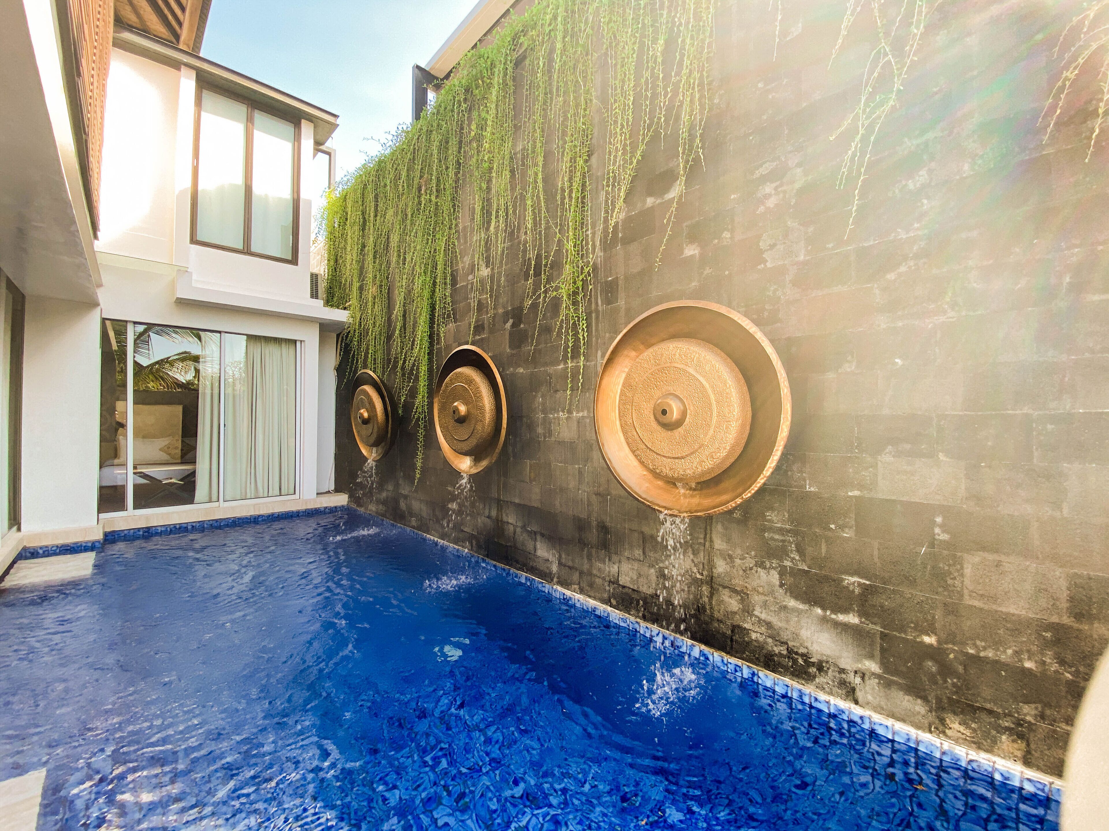 A swimming pool with a blue tiled floor and a wall with hanging plants and water features.