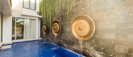 A swimming pool with a blue tiled floor and a wall with hanging plants and water features.