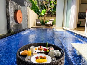 A breakfast setup on a floating platform in a pool area with a stone wall and greenery in the background. - Puri Hiromi (Denpasar)