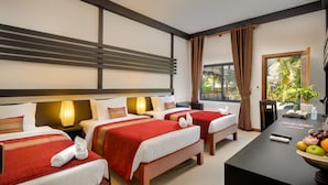 A hotel room with two beds, a desk with a bowl of fruit, and a view of greenery outside. - Reveal Courtyard in Reveal Angkor (Siem Reap)